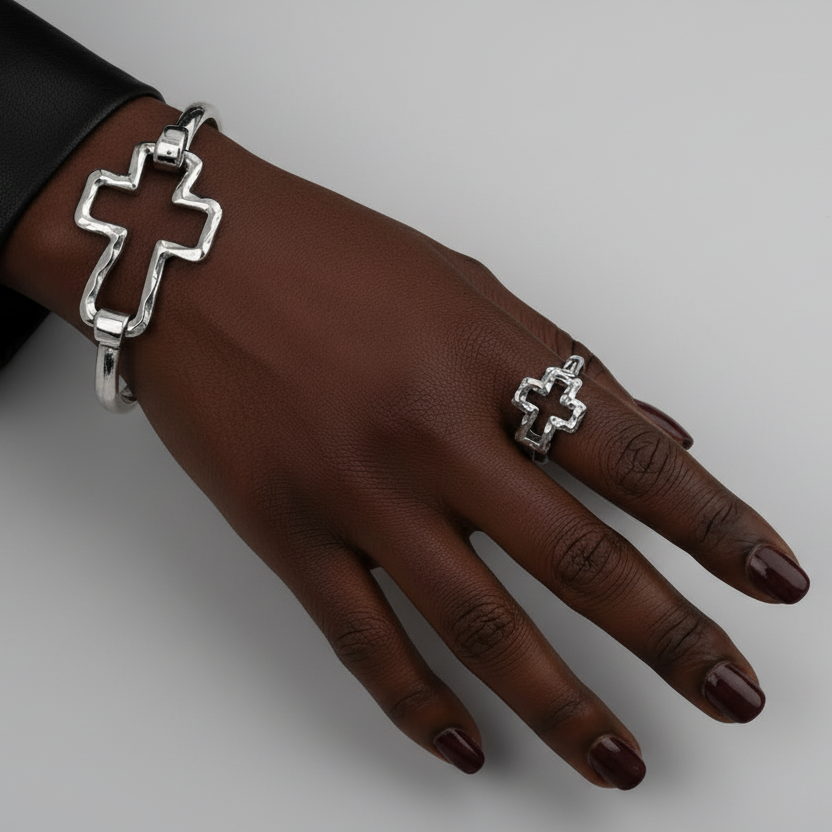 Hand wearing a silver cross bracelet and ring on a neutral background