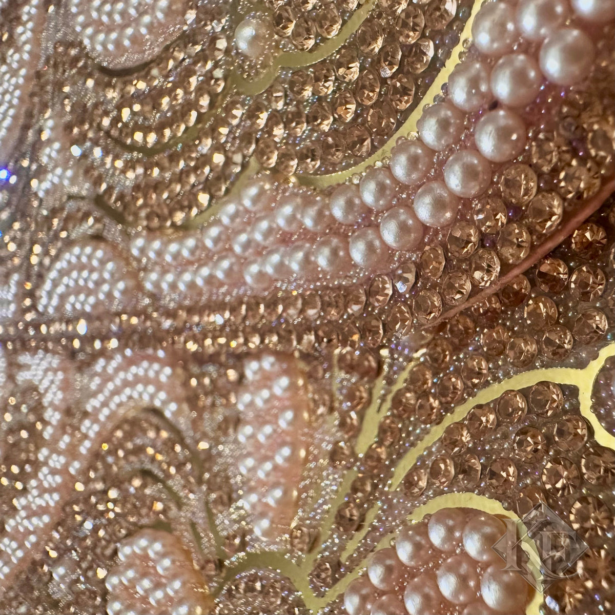 Close-up of an ornate embellished surface with rows of white faux pearls, rhinestones, and metallic gold curved lines over a warm beige base.
