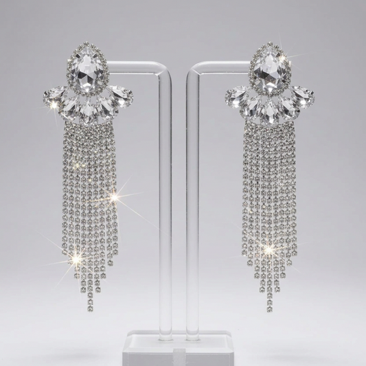 Pair of ornate earrings with dangling crystals on a clear stand against a gray background