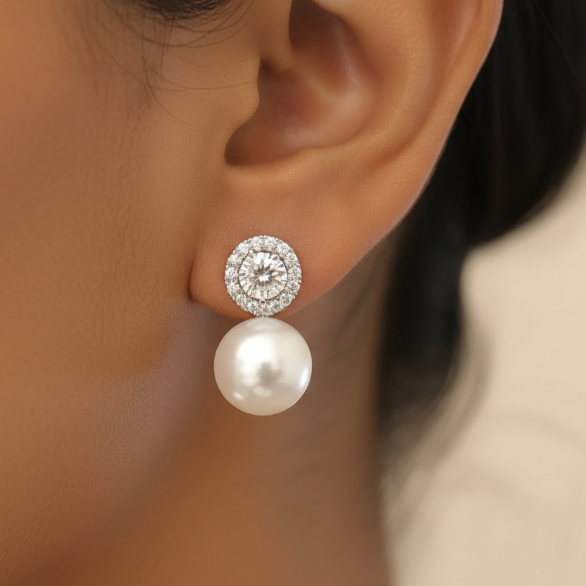 Pearl earring with silver clasp worn on an ear against a neutral background