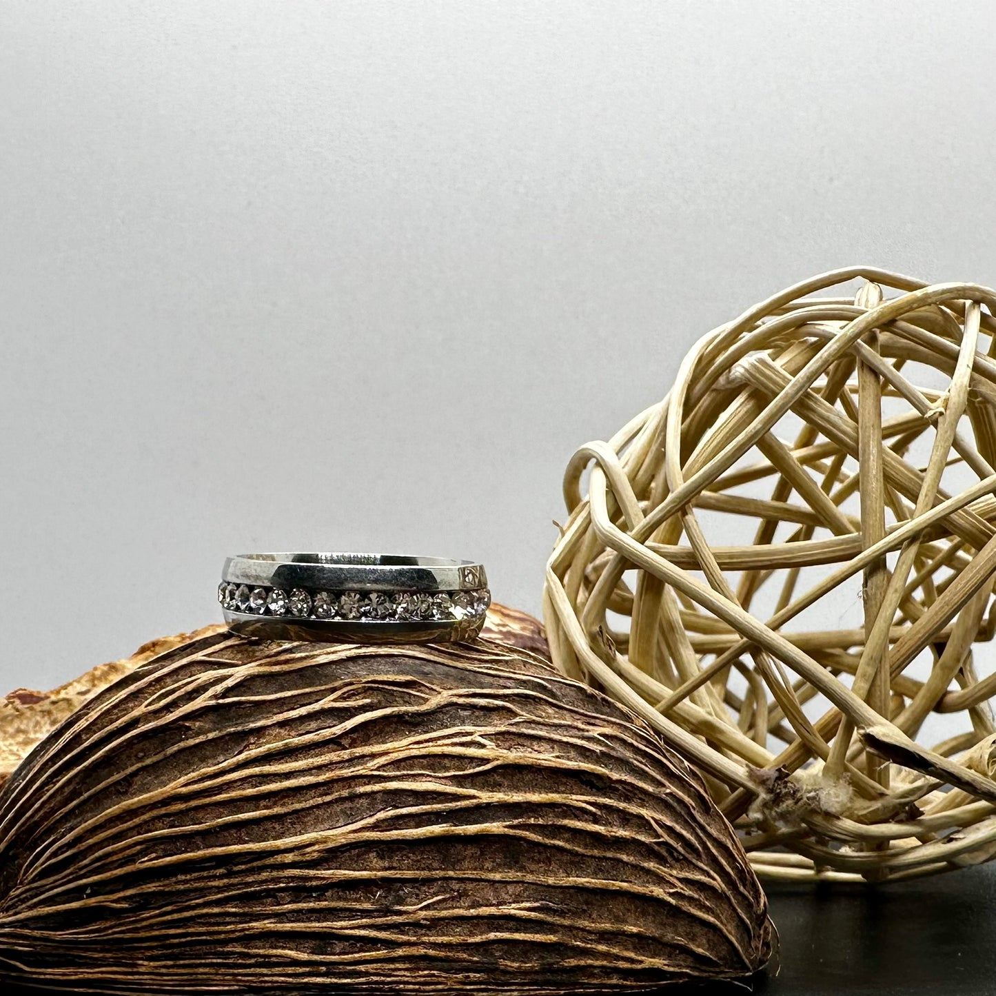 Silver ring with gemstones on a textured surface next to a woven ball.