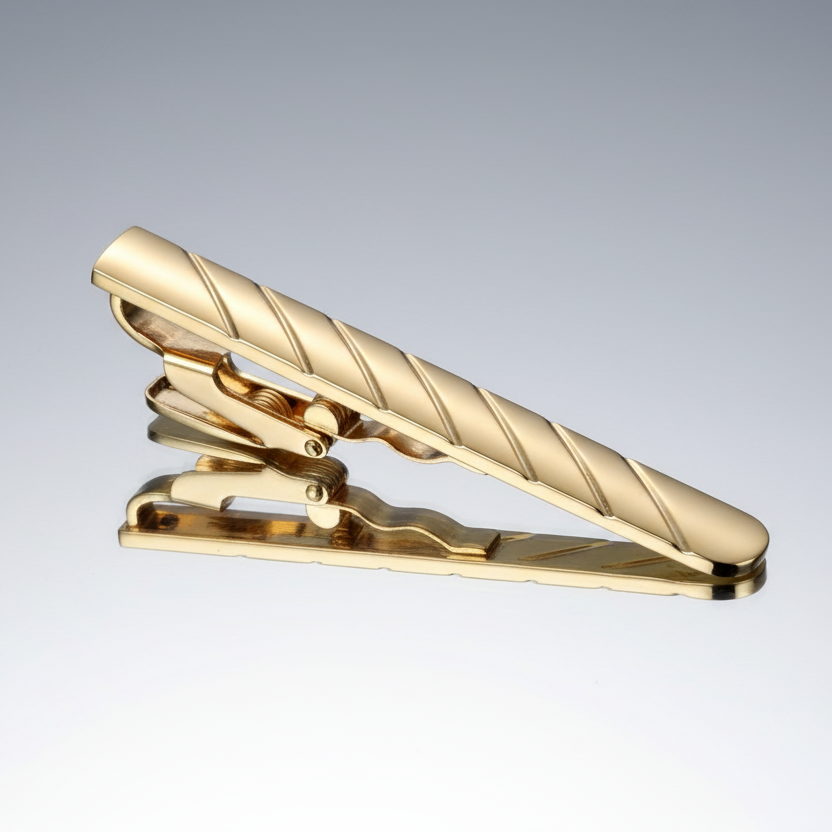 A gold tone tie clip with elegant stripes design, positioned diagonally.