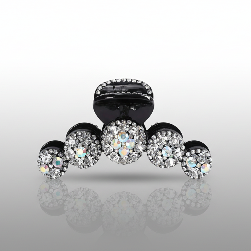 Black hair clip with crystal embellishments on a reflective gray surface