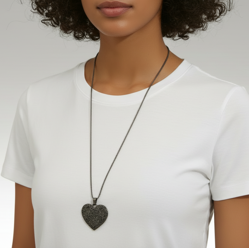 Person wearing a white t-shirt and a necklace with a heart-shaped pendant on a plain background