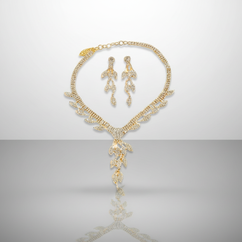 Gold necklace and earrings set on a reflective surface with a gray background