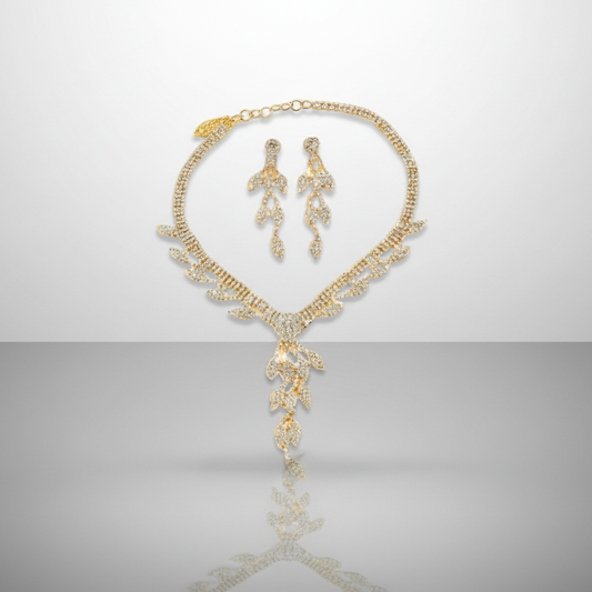 Gold necklace and earrings set on a reflective surface with a gray background