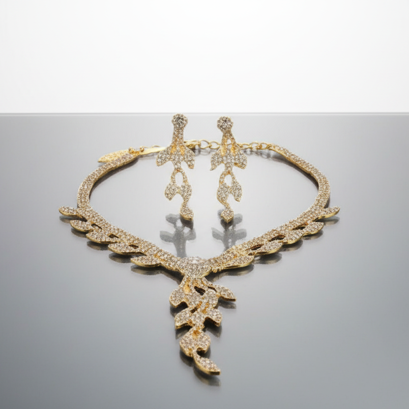 Gold necklace and earrings on a reflective surface with a gray background