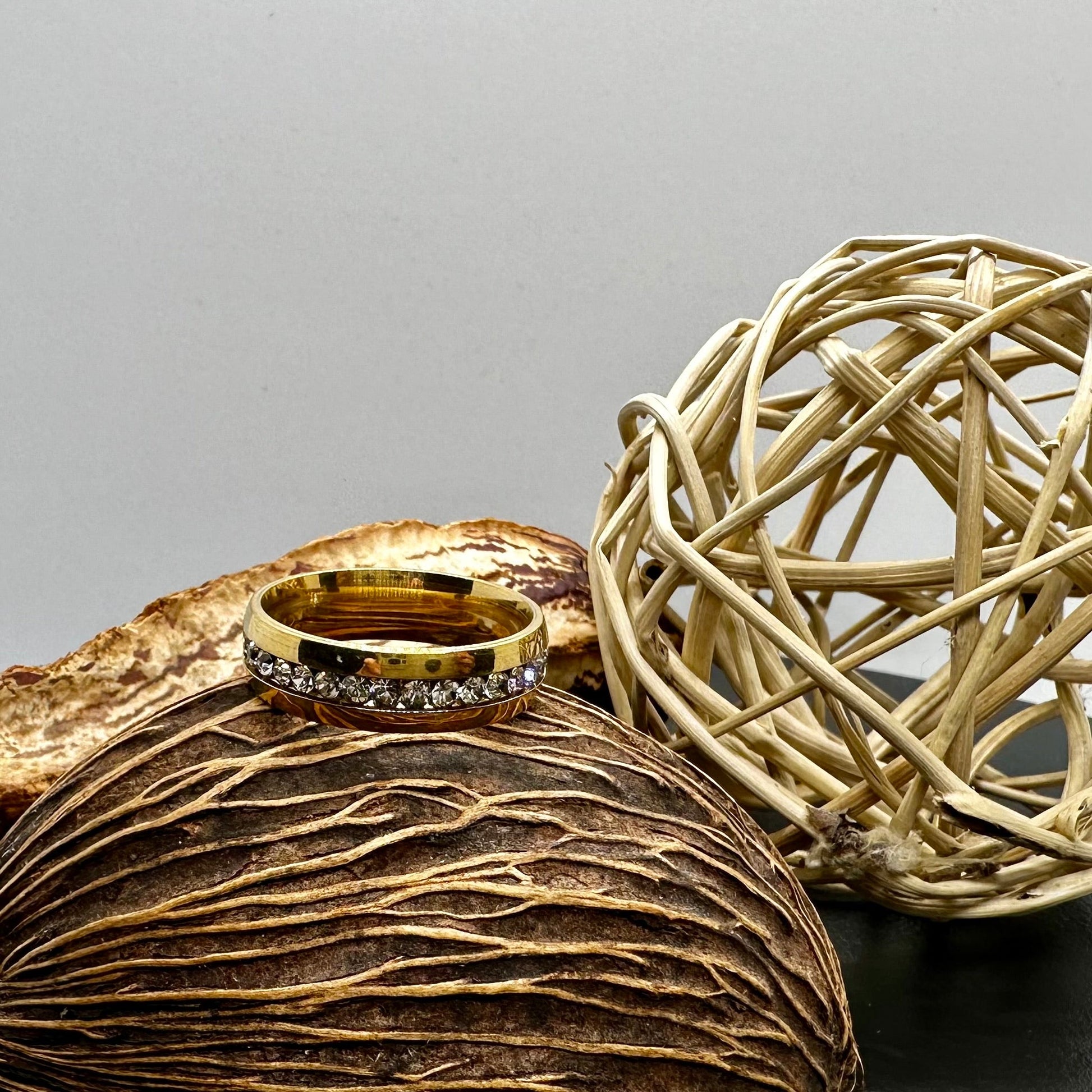 Gold ring with faux diamonds on a textured surface next to a woven ball.