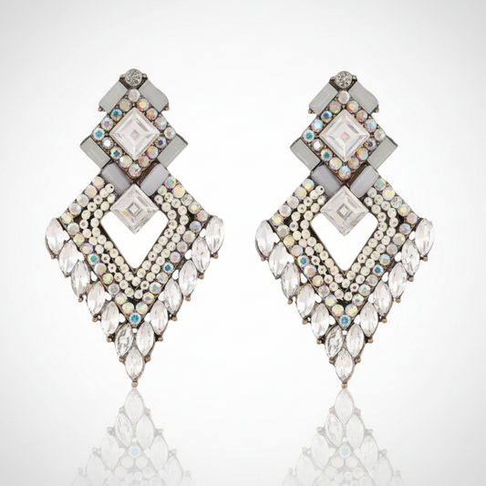 Pair of diamond-shaped earrings with gemstones on a reflective surface.