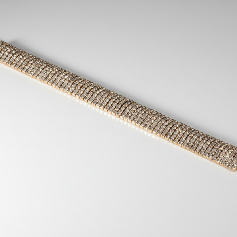 Close-up of a gold bracelet with clear stones on a light gray background