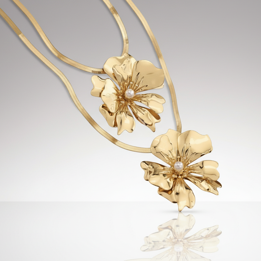Gold floral necklace with pearl centers on a reflective surface