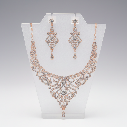 Rose gold necklace and earrings set on a white stand with a gray background