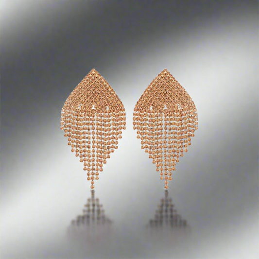 Pair of champagne gold earrings on a reflective surface with a gradient background