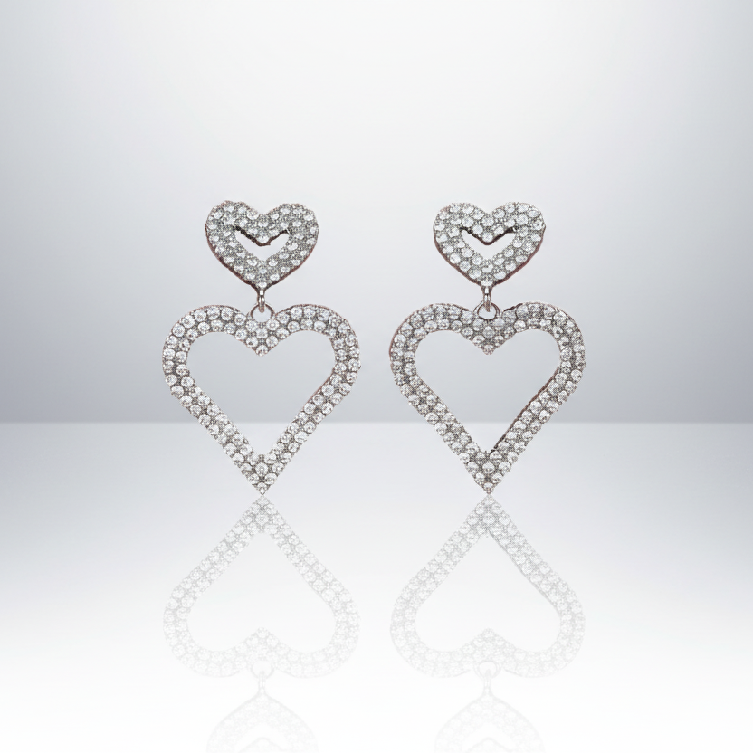 Heart-shaped earrings with diamond-like stones on a reflective surface.