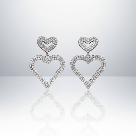 Heart-shaped earrings with diamond-like stones on a reflective surface.