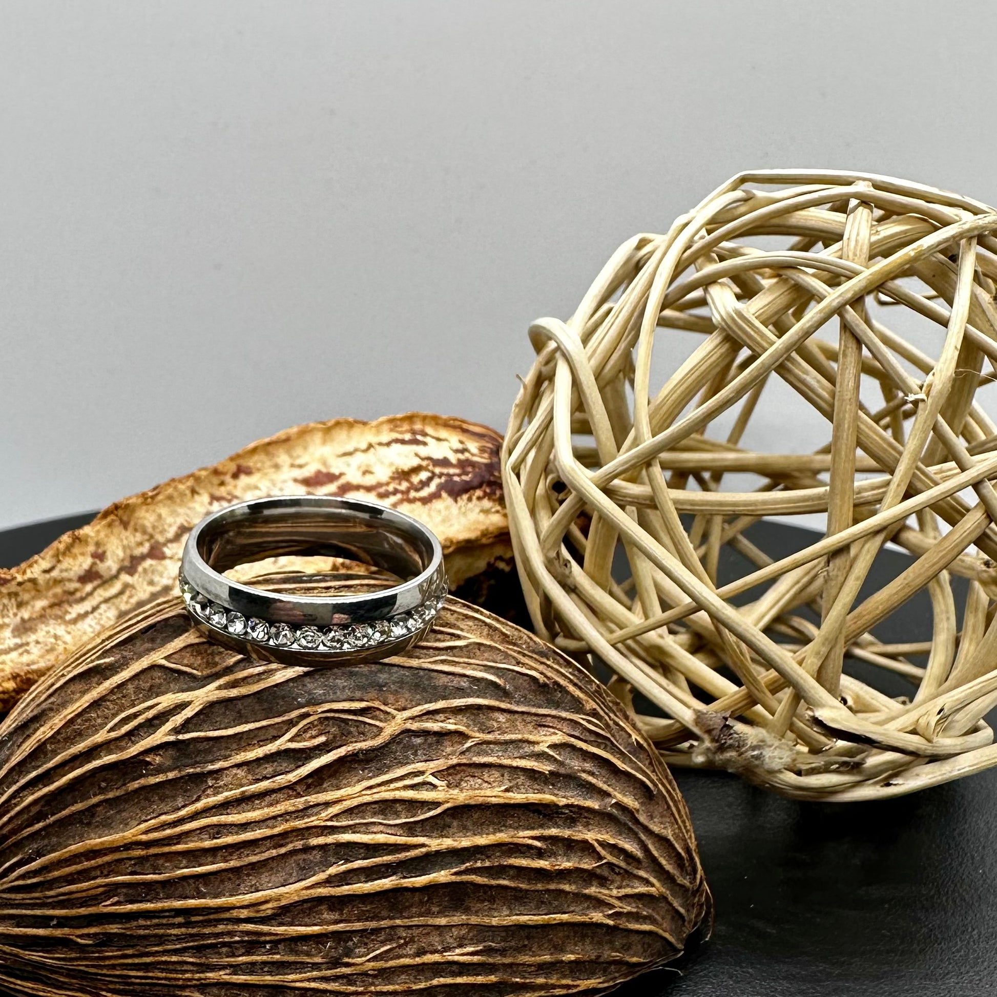 Silver ring on a textured surface with a woven ball in the background