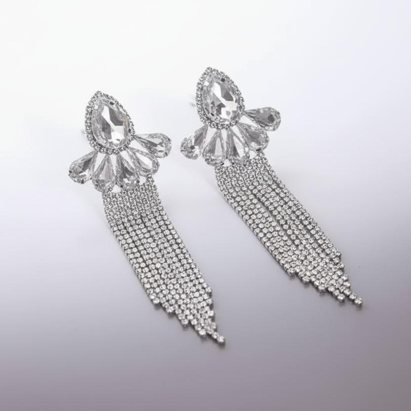 Pair of silver earrings with teardrop-shaped crystals and dangling chains on a light gray background