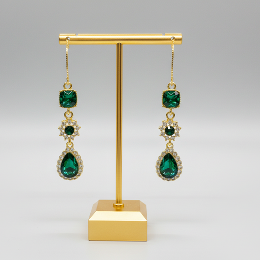 Gold earrings with green gemstones on a gold stand against a white background