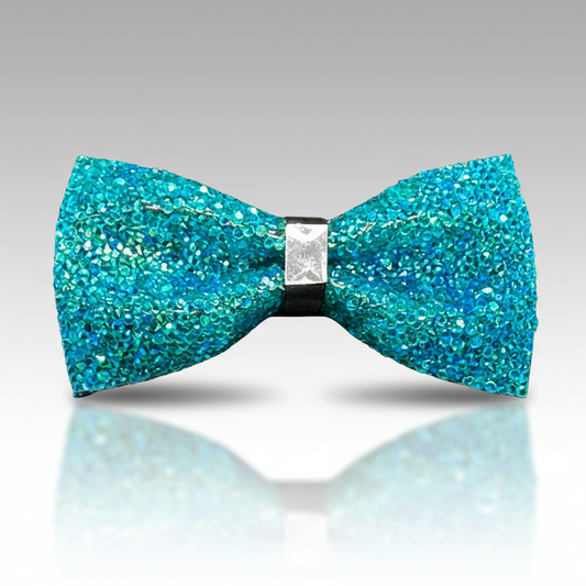 Turquoise glitter bow tie on a reflective surface with a gray background