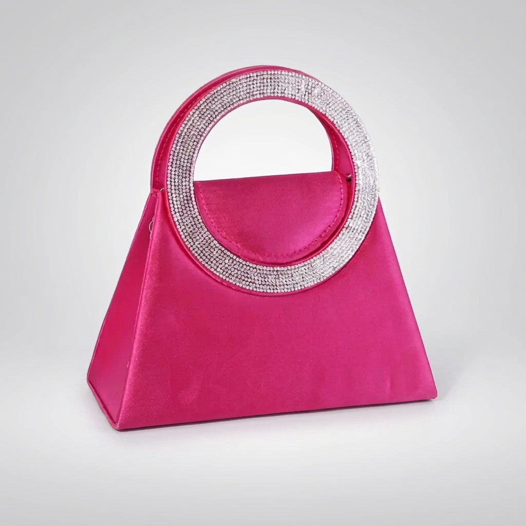 A hot pink satin handbag with a structured triangular shape and a large circular top handle encrusted with silver rhinestones, shown on a grey and white background.