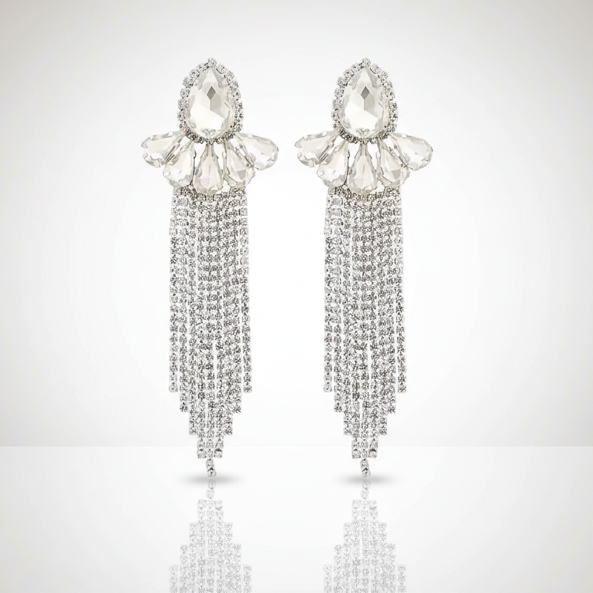 Pair of silver earrings with teardrop-shaped crystals and dangling chains on a light gray background