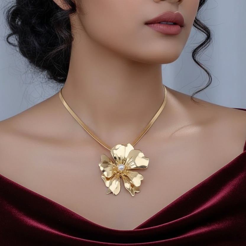 Gold necklace with a floral design worn by a person in a burgundy top against a gray background