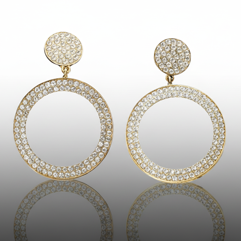Gold hoop earrings with clear gemstones on a reflective surface