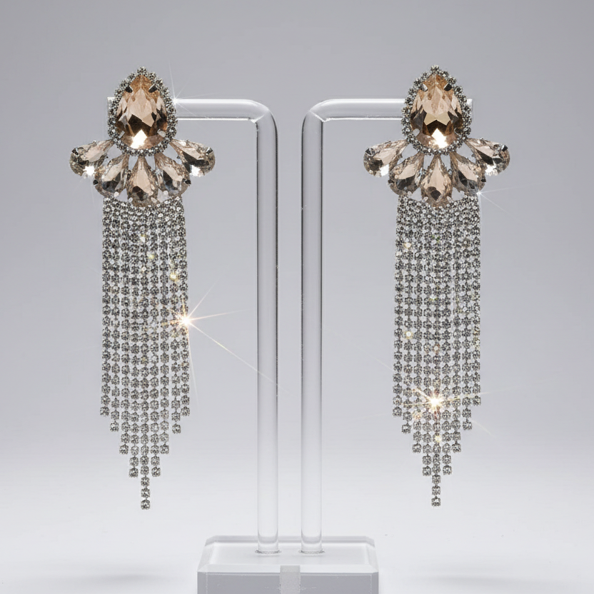 Pair of ornate earrings with dangling crystals on a clear stand against a gray background